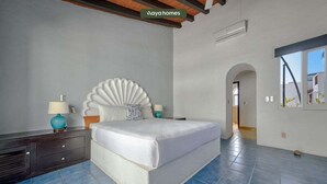 A bedroom with a large bed, a decorative headboard, a nightstand with a lamp, and a view of the outside through a window. - Cozy 3BR House Perfect for Families - Pool (Nuevo Vallarta)
