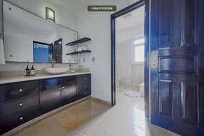 A modern bathroom with a large mirror, a white sink, dark cabinets, and a blue door.