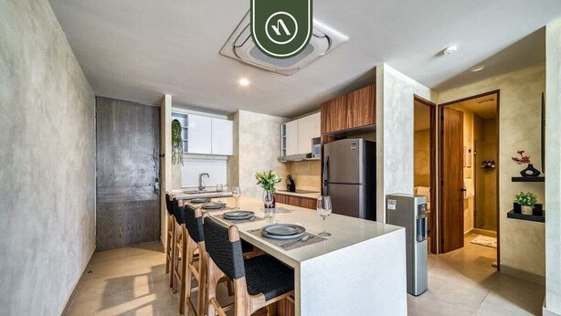 A modern kitchen with a central island, wooden chairs, a refrigerator, and a water dispenser.