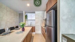 A modern kitchen with a stainless steel refrigerator, wooden cabinets, and a marble countertop.