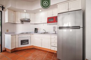 A kitchen with white cabinets, a stainless steel refrigerator, a red microwave, and a built-in oven.