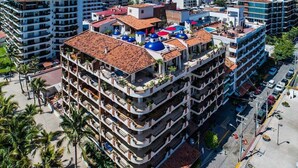 Ein mehrstöckiges Hotel mit Balkonen, einer Dachterrasse und einem Parkplatz.