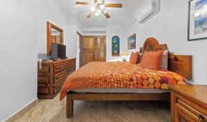 Une chambre avec un lit en bois, un ventilateur de plafond, une télévision et une armoire.