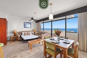 A hotel room with a balcony, a dining area, a sofa set, and a bed.