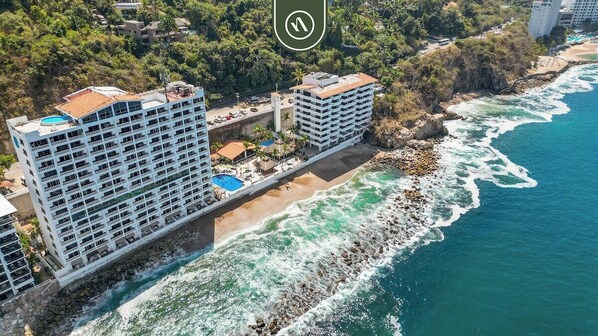 A coastal hotel with multiple balconies, a pool, and a beachside location.