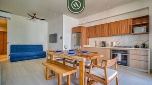 A modern kitchen with wooden cabinets, a built-in microwave, and a dining area with a wooden table and benches. - New 1 BR Condo with Amazing Rooftop Pool - Jacuzzi (Bucerías)