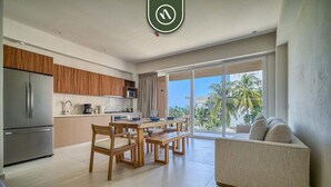 A modern kitchen with a dining area, a sofa, and a view of palm trees. - New 1 BR Condo with Amazing Rooftop Pool - Jacuzzi (Bucerías)