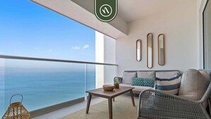 Ein Balkon mit Blick auf den Ozean, eine Couch, ein Korbstuhl, ein kleiner Tisch mit einer Schale und drei Wandspiegel.