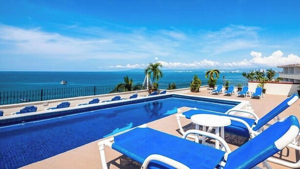A pool area with blue lounge chairs and a view of the ocean. - Cozy 2BR King beds - Rooftop Pool - Fast WiFi (Puerto Vallarta)
