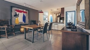 A modern kitchen with a central island, a dining area with a wooden table and chairs, and a large abstract painting on the wall. - Cozy 2BR King beds - Rooftop Pool - Fast WiFi (Puerto Vallarta)