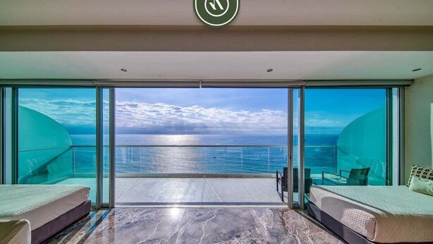 A modern room with a large glass door leading to a balcony with a sea view.