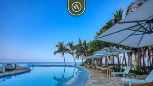 A poolside area with lounge chairs and umbrellas, a clear view of the ocean, and a tiled walkway.