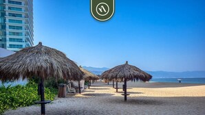 A beach with thatched umbrellas and a clear view of the ocean.