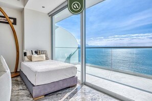A bedroom with a bed, a large window, and a view of the sea.