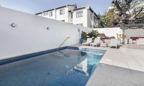 A swimming pool with a metal ladder, white lounge chairs, and potted plants.