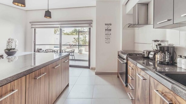 A modern kitchen with wooden cabinets, a large island, and a view to an outdoor patio. - DellaTerra 1A | 2BR/2BA Nuevo Nayarit | Pool & WiFi (Bucerías)