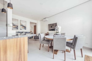 Une cuisine moderne avec un îlot central en bois, des chaises à revêtement gris et des œuvres d’art accrochées aux murs.