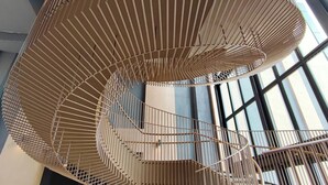 Een spiraaltrap met een metalen leuning en een grote, geometrische, zwevende constructie op de achtergrond.