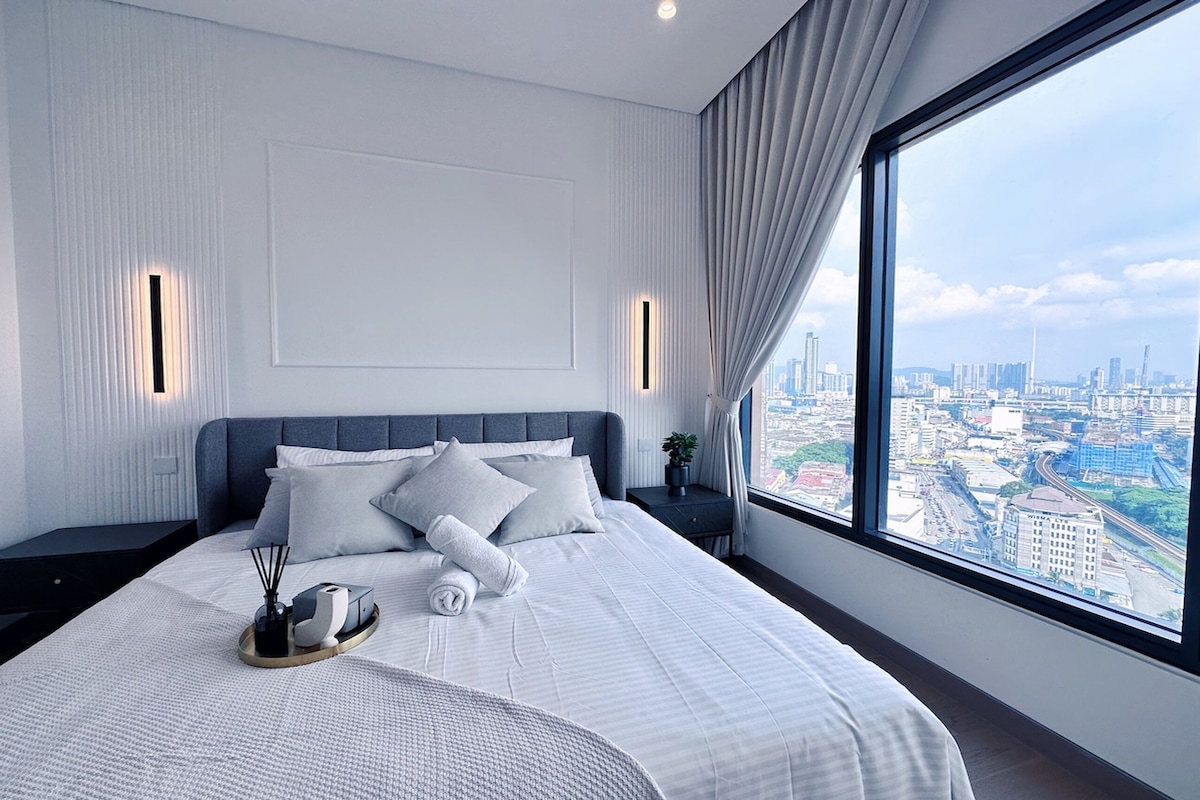 A modern hotel room with a large bed, city view, and a nightstand with a lamp.