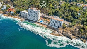 A coastal hotel with multiple floors, a swimming pool, and a view of the ocean.