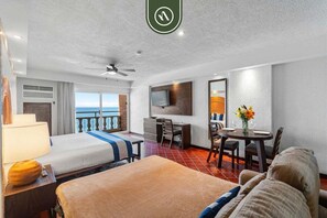 Quarto de hotel com cama, escrivaninha, cadeira, mesa de jantar, televisão e varanda com vista.