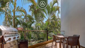 Un patio exterior con una parrilla, una mesa y sillas, y vistas a palmeras.