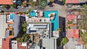 Vista aérea de un hotel con piscina, tumbonas y una zona de estar cubierta.