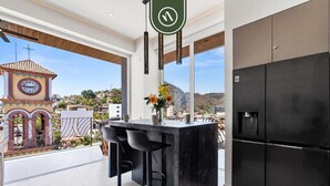 Een moderne keuken met een zwarte koelkast, een bar met barkrukken en uitzicht op een klokkentoren en bergen.