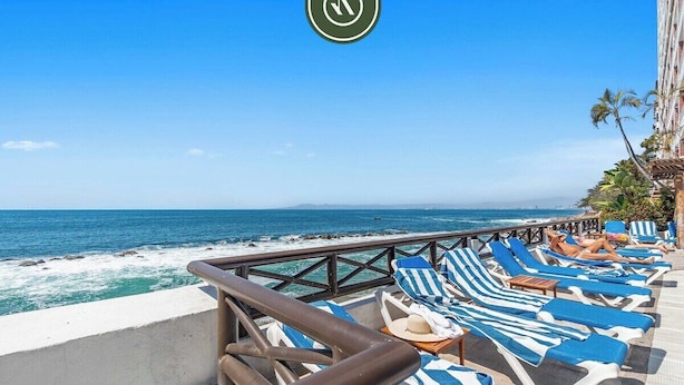 A seaside balcony with blue and white striped lounge chairs, a railing, and a view of the ocean.