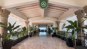 A hotel lobby with a wooden floor, columns, and potted plants.