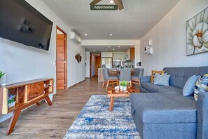 Uma sala de estar moderna com um sofá cinza, mesa de centro de madeira e uma TV fixada na parede.