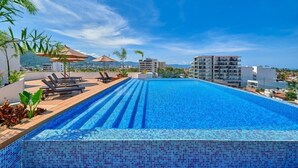 A rooftop infinity pool with lounge chairs, umbrellas, and a view of the cityscape. - Brand New 2BR Apt - Infinity Pool - Versalles (Puerto Vallarta)
