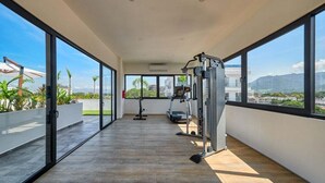 A spacious balcony with a gym area, large windows, and a view of the city and mountains. - Brand New 2BR Apt - Infinity Pool - Versalles (Puerto Vallarta)