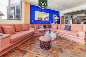 Habitació amb un sofà seccional rosa, una taula de centre rodona, un tamboret de pedra i un mirall gran, amb una paret d'accent blava.