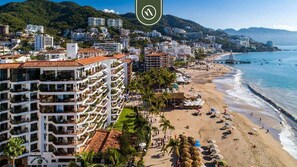 Ein Hotel an der Küste mit mehreren Balkonen, einem Strand und einer Bergkulisse.
