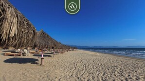 A beach with thatched umbrellas and wooden lounge chairs. - Playa Royale Tower 1 1133 | 1BR Nuevo Vallarta | Beach, pool & WiFi (Nuevo Vallarta)