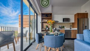 A modern kitchen with a microwave, refrigerator, and wooden cabinets. There is a dining area with a glass table and blue chairs. - Oasis-810 | 1BR/1BA Puerto Vallarta | Pool & Gym (Puerto Vallarta)