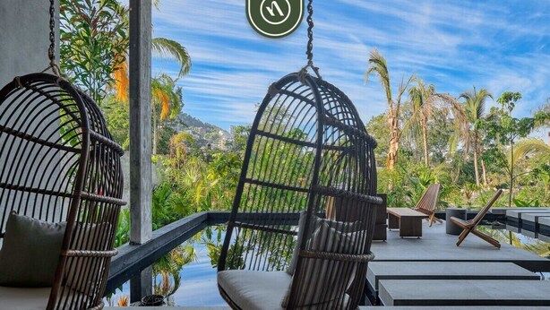 A balcony with wicker chairs and a view of a tropical landscape. - Oasis-810 | 1BR/1BA Puerto Vallarta | Pool & Gym (Puerto Vallarta)