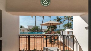 Un balcón con vista a la piscina, mobiliario exterior y barandilla.