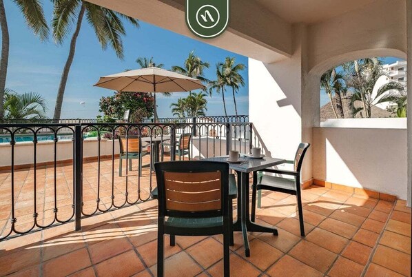 Eine Terrasse mit Tisch und Stühlen und Blick auf den Strand, gesäumt von Palmen.