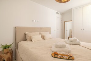 Un dormitorio con una cama grande, una mesita de noche con una planta y una bandeja con toallas y un cesto.