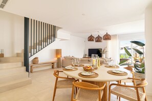 Un salon moderne avec un coin repas, comprenant un escalier, des meubles en osier et une grande fenêtre offrant une vue dégagée.