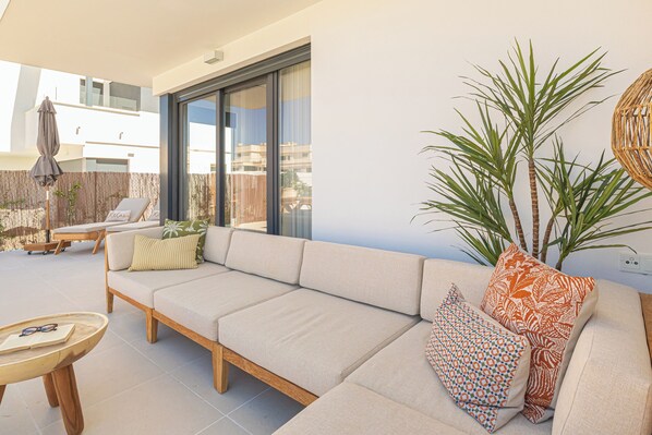Una sala de estar moderna con un sofá color beige, cojines estampados, una mesa de centro de madera y un ventanal con vistas a edificios.