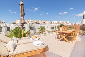Una terraza en la azotea con un sofá, una mesa y una sombrilla.