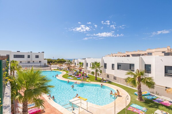 Un área de piscina con varias piscinas, sillas de descanso y palmeras.