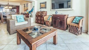 A spacious living room with a glass coffee table, wicker furniture, and a large TV. - 805-VistadelSol | 2BR/2BA PV, beach, pool, AC (Puerto Vallarta)