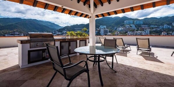 An outdoor patio with a grill, chairs, and a table. - 805-VistadelSol | 2BR/2BA PV, beach, pool, AC (Puerto Vallarta)