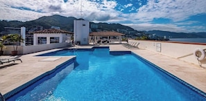 Ein Pool auf dem Dach mit klarem, blauem Wasser, Liegestühlen und Bergblick.