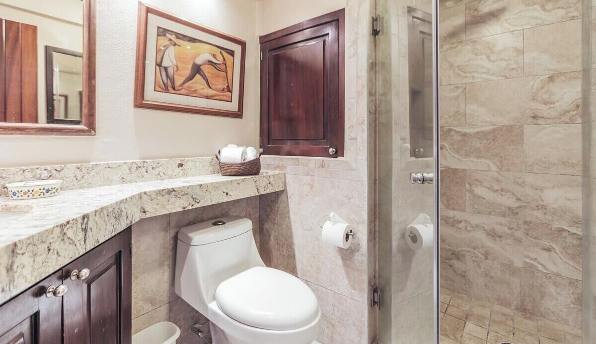 Une salle de bain avec des toilettes, un lavabo et une douche. Un tableau encadré est accroché au mur et un meuble en bois se trouve au-dessus du lavabo.