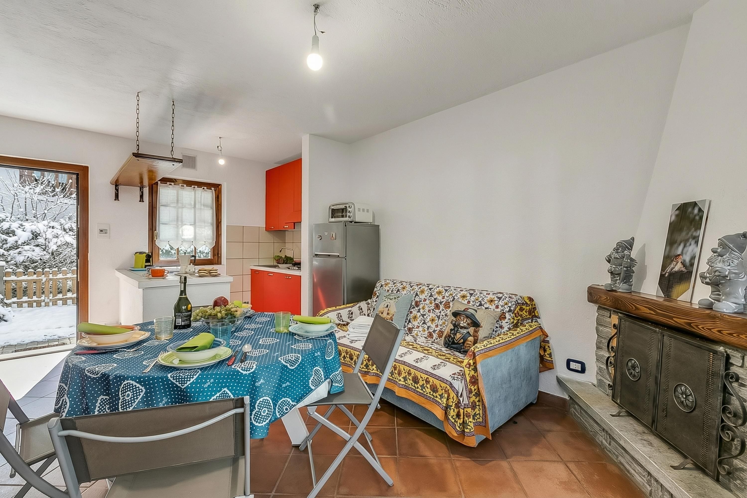 A dining area with a table set for two, a sofa, and a kitchen in the background.